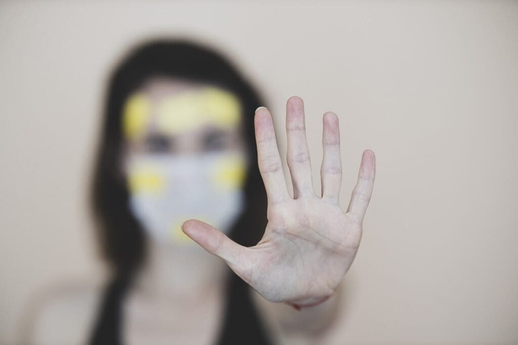 Blurred shot of woman in covid mask holding up her palm to camera