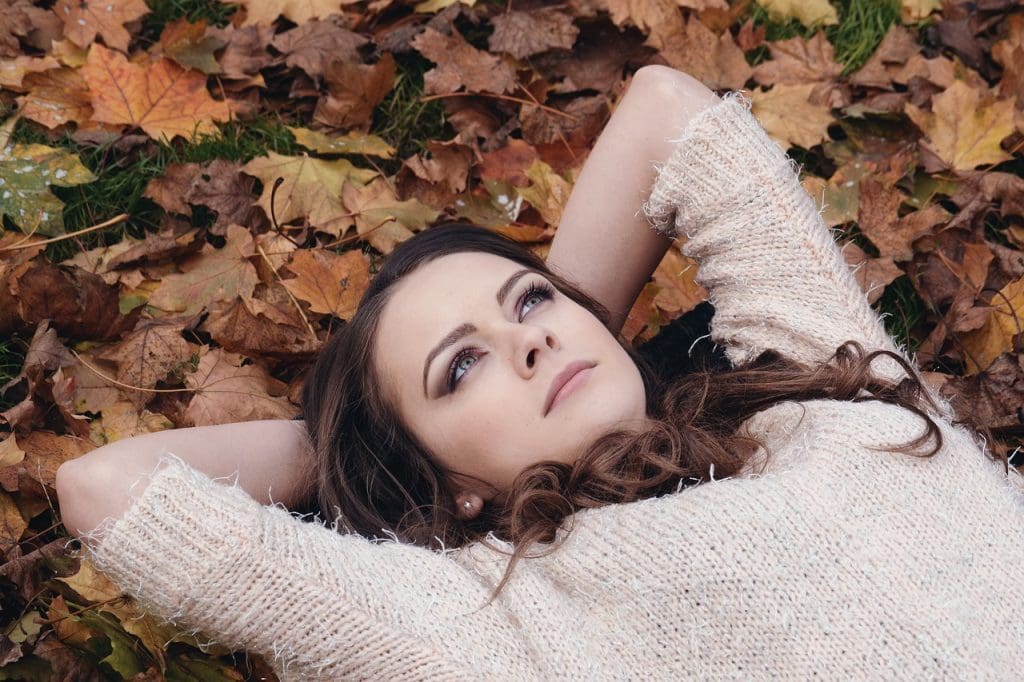 Brunette woman lying on bed of leaves, thinking